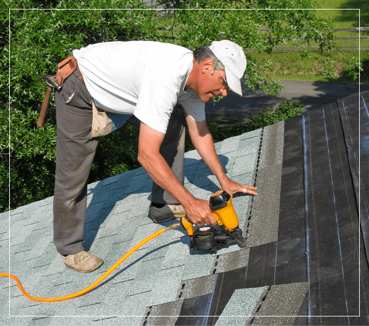 Man using nail gun on roof shingles.